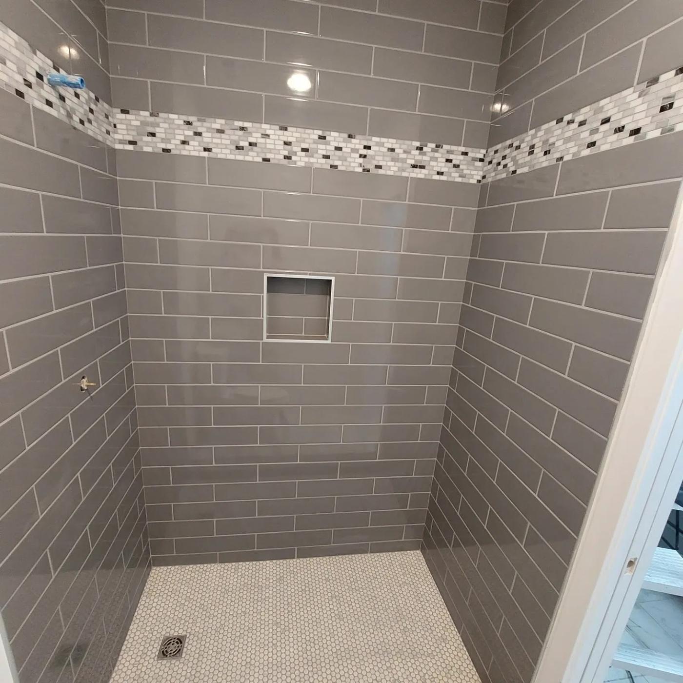 Grey subway tiled shower with a mosaic accent band, recessed niche and a small round mosaic floor