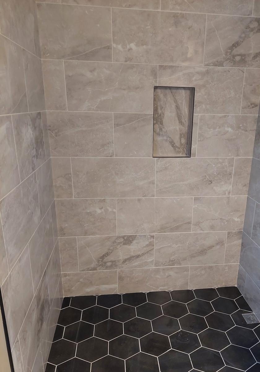 Marble look tiled shower with a black hexagon tile floor and a recessed niche
