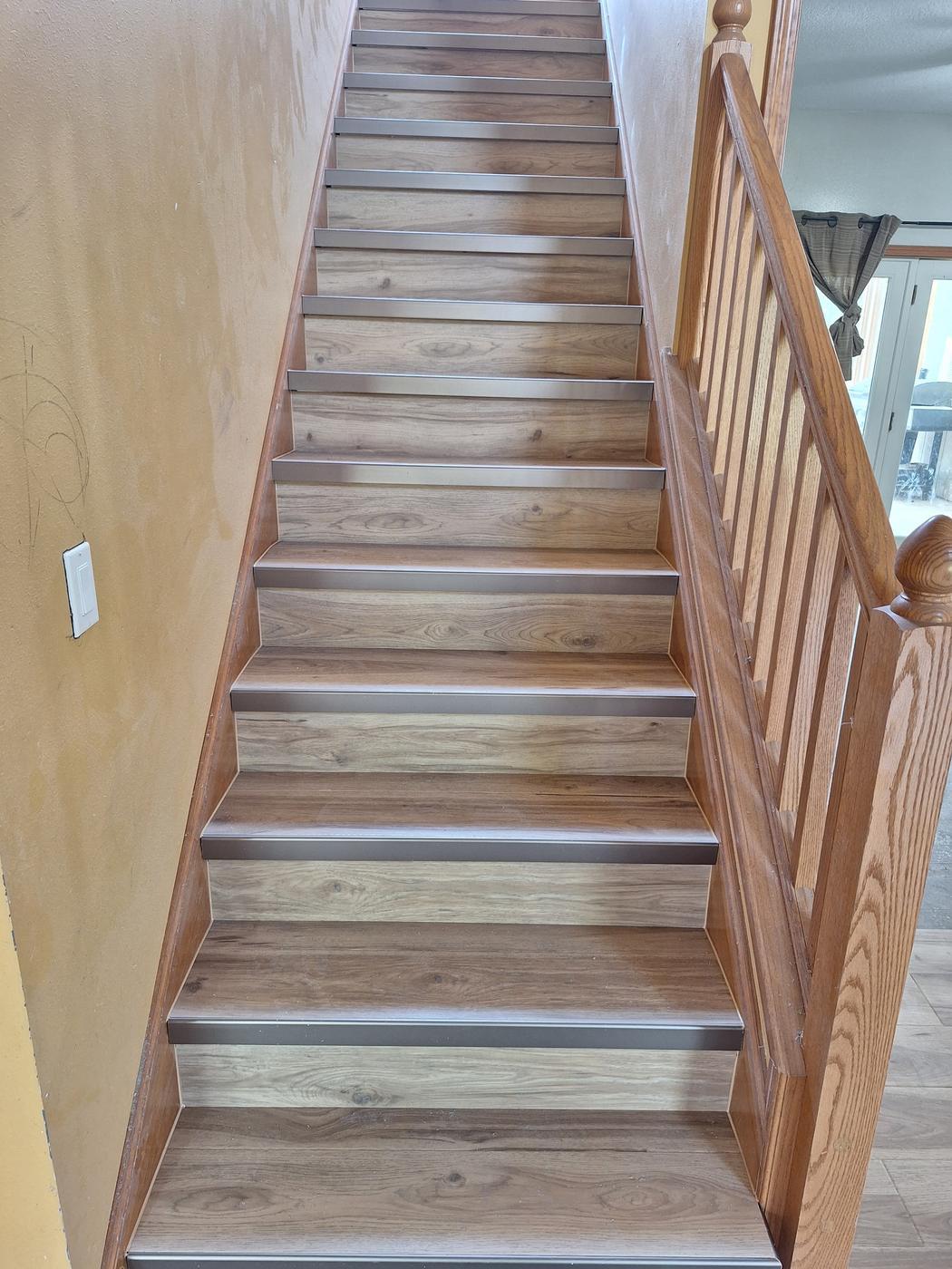 Staircase with treads and risers finished with metal nosings, beside an oak balustrade