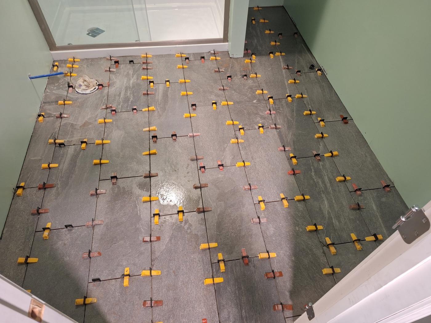 A tile floor part way through installation with leveling clips and wedges still in place between the tiles
